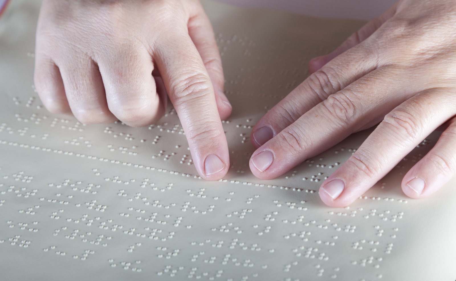 Hands reading a sheet of embossed braille.