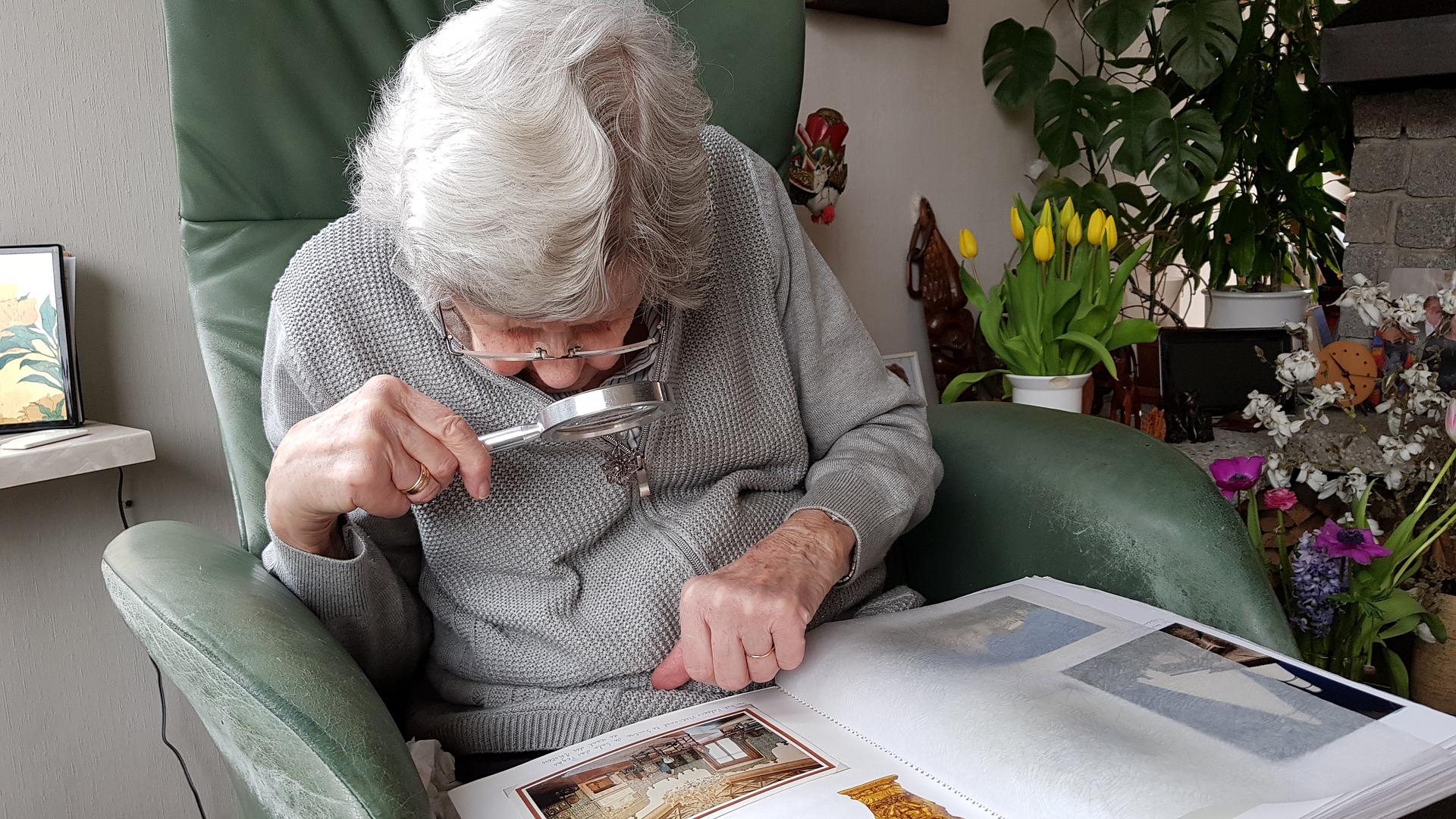 A person with low vision sitting in a chair using a handheld magnifier.