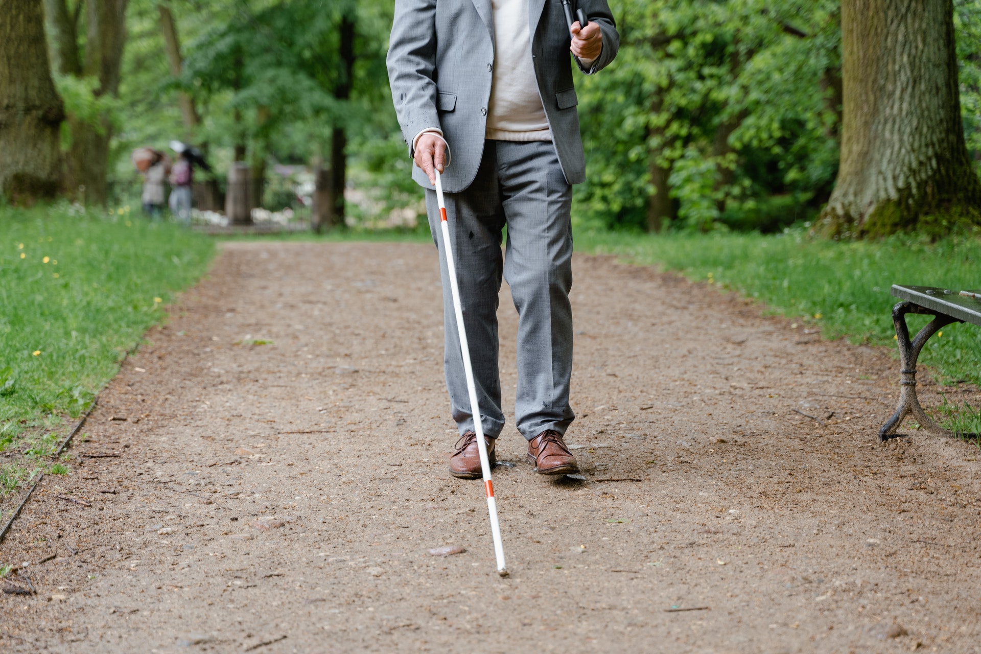 A man walking down a path with a white mobility cane.